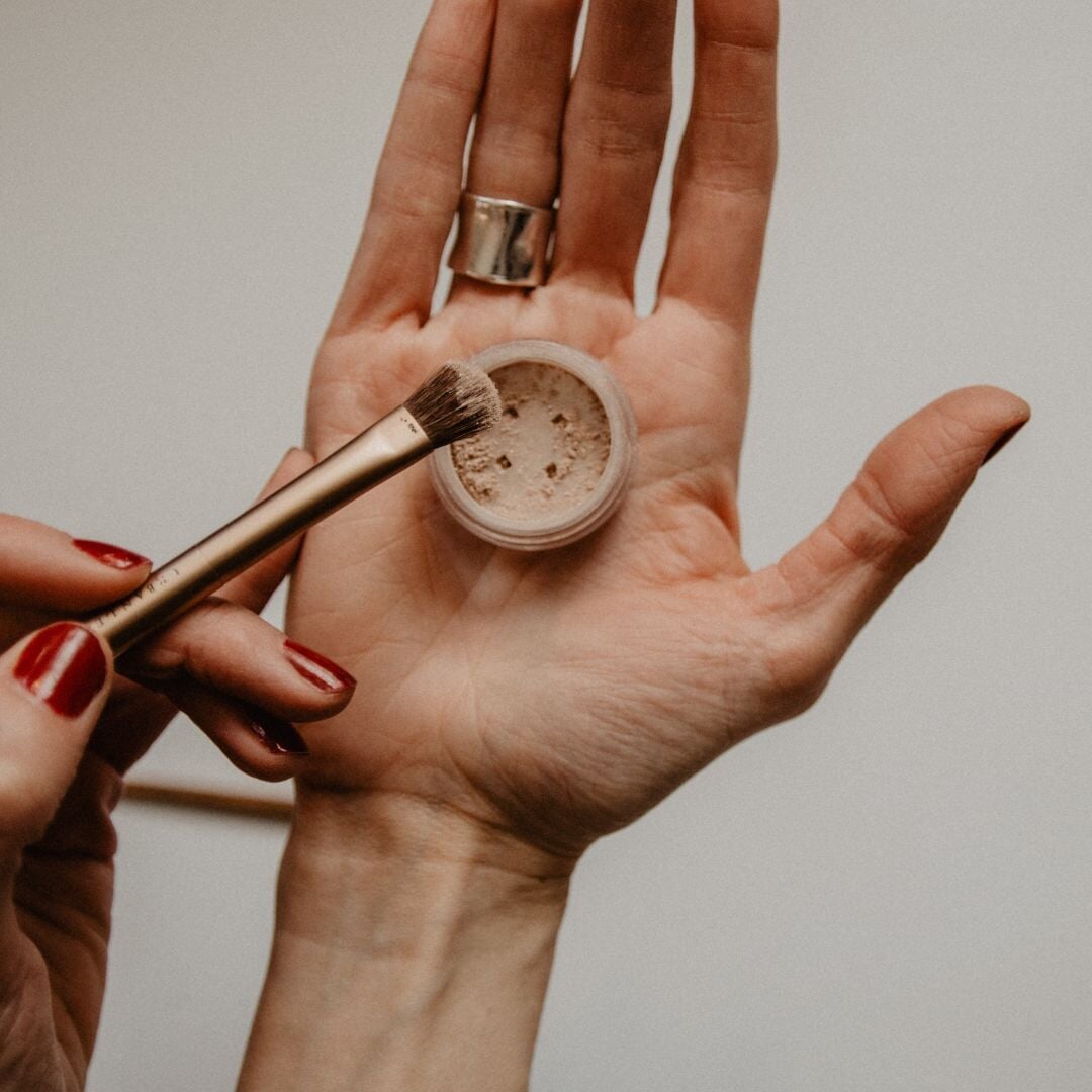 hand holding an open container of mineral makeup with brush