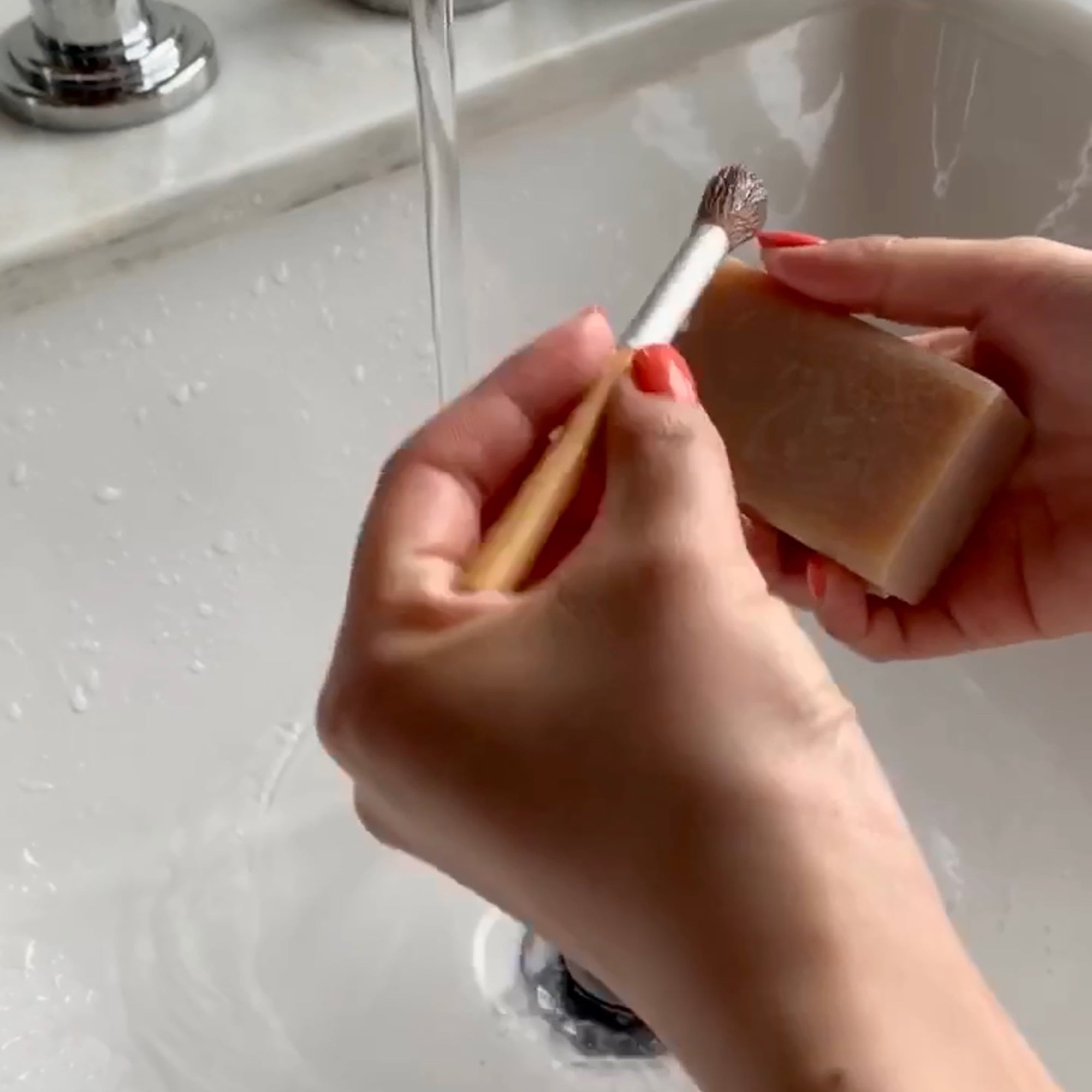 woman holding makeup brush in sink with the other hand holding a bar of soap