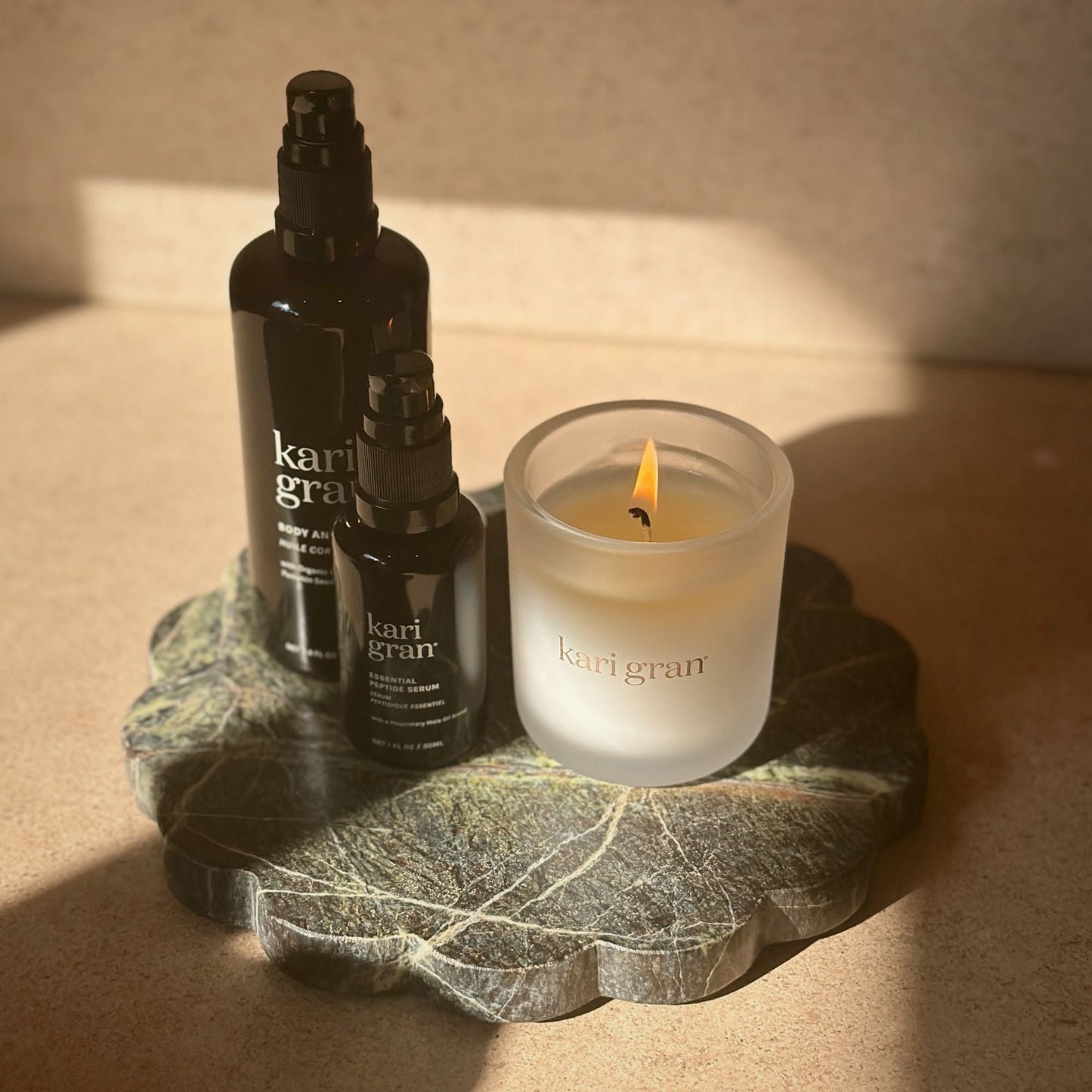 Image of kari gran candle, essential peptide serum and body and bath oil on top of green marble plate