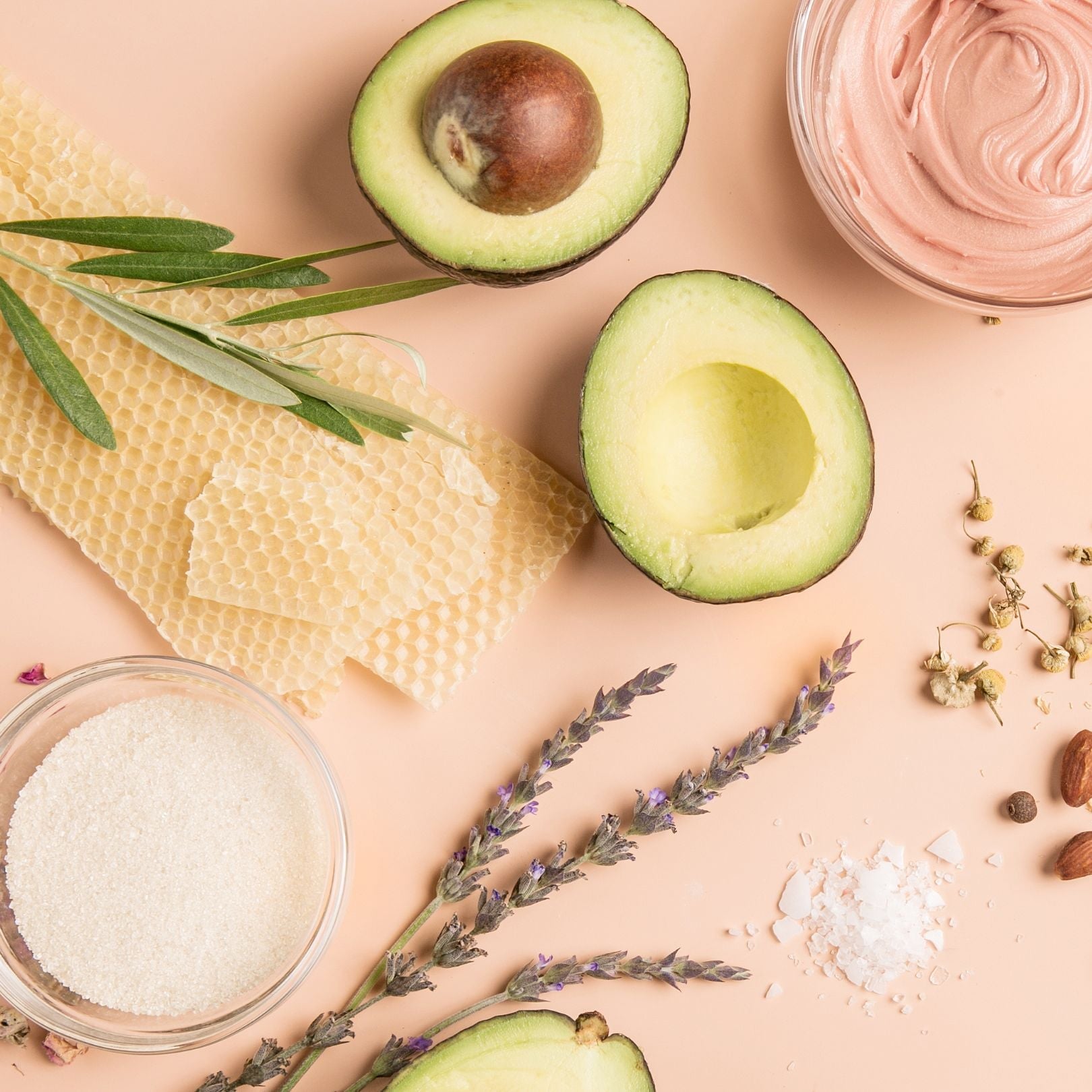 skin care ingredients including avocados, beeswax, and lavender on a pink background