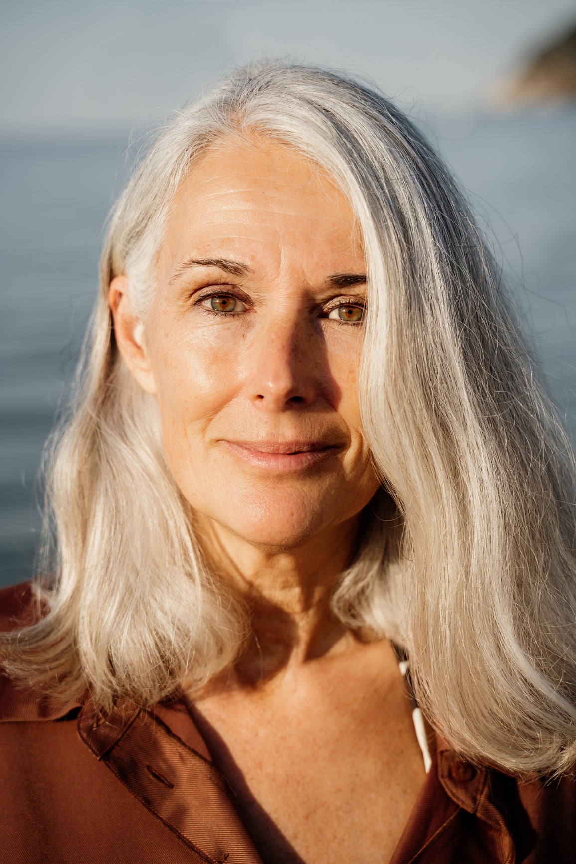 Woman with gray hair standing against a blurred natural background