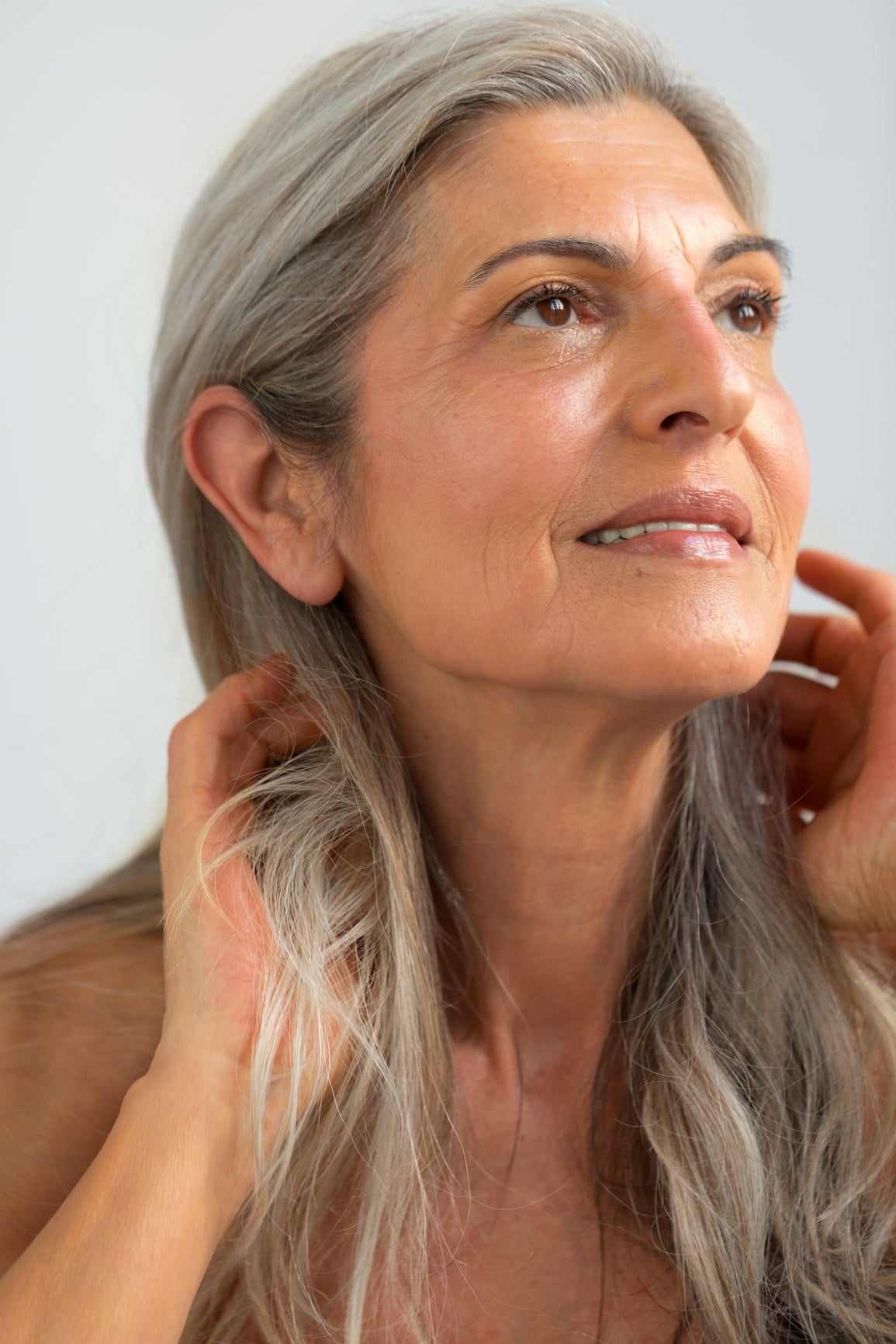 Woman with gray hair touching her face against a light background