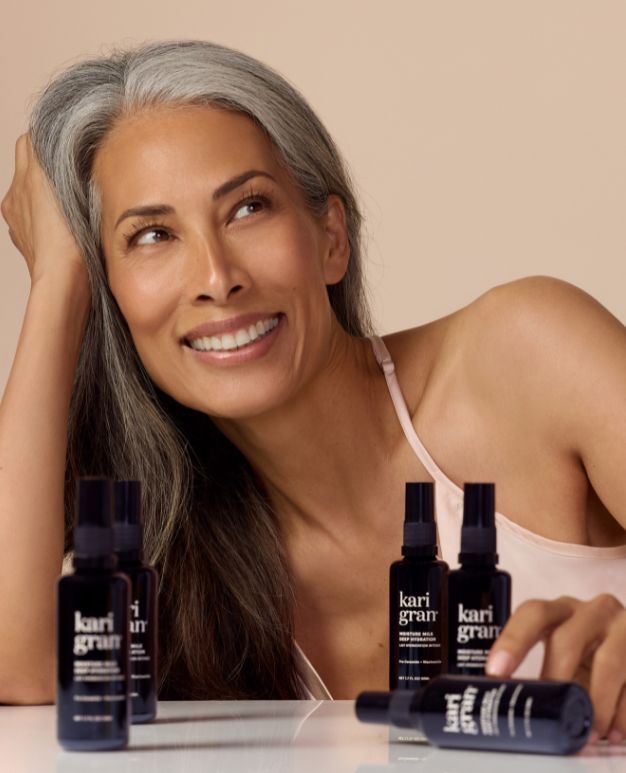 Woman with gray hair sitting next to Kari Gran products on a beige background